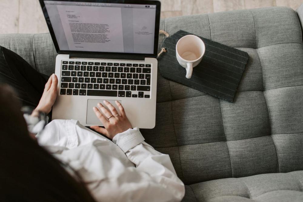 5. Cum se face corect o lucrare  de licenta - femeie asezata pe canapea, laptop, cana de cafea