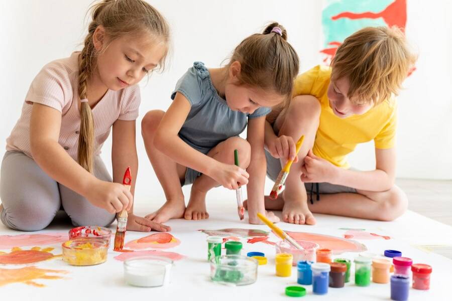 2. Activitati de grup pentru copii - tipuri de activitati potrivite in grup si echipe, in functie de varsta si locul unde se desfasoara_Copiii care picteaza impreuna, tempera, pensule, plansa