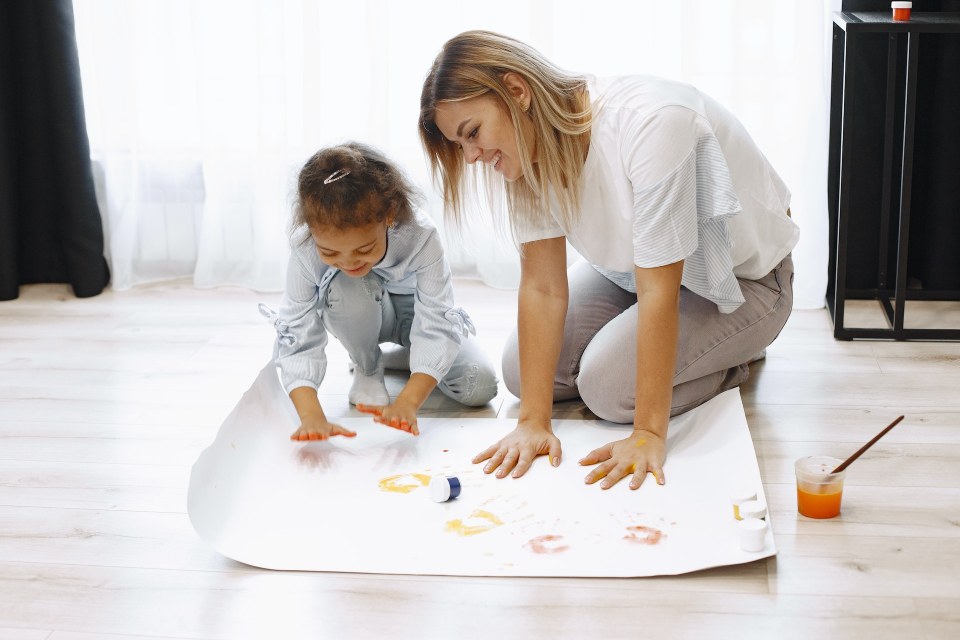 2. Idei de pictura pentru copii - tehnici pentru toate vârstele - mama si fetita, isi picteaza mainile pe o coala mare, pe podea